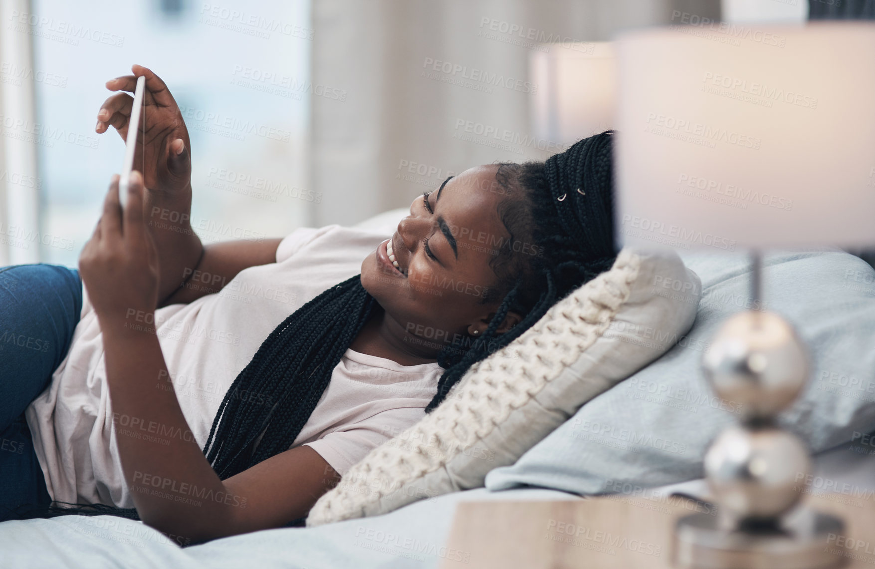 Buy stock photo Shot of a young woman using a digital tablet while relaxing on her bed at home