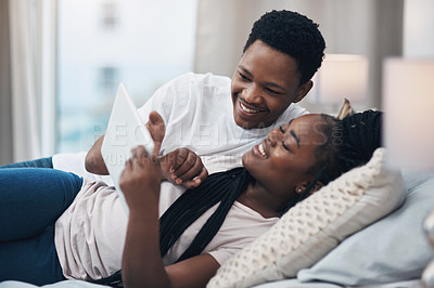Buy stock photo Shot of a young couple using a digital tablet while relaxing on their bed at home