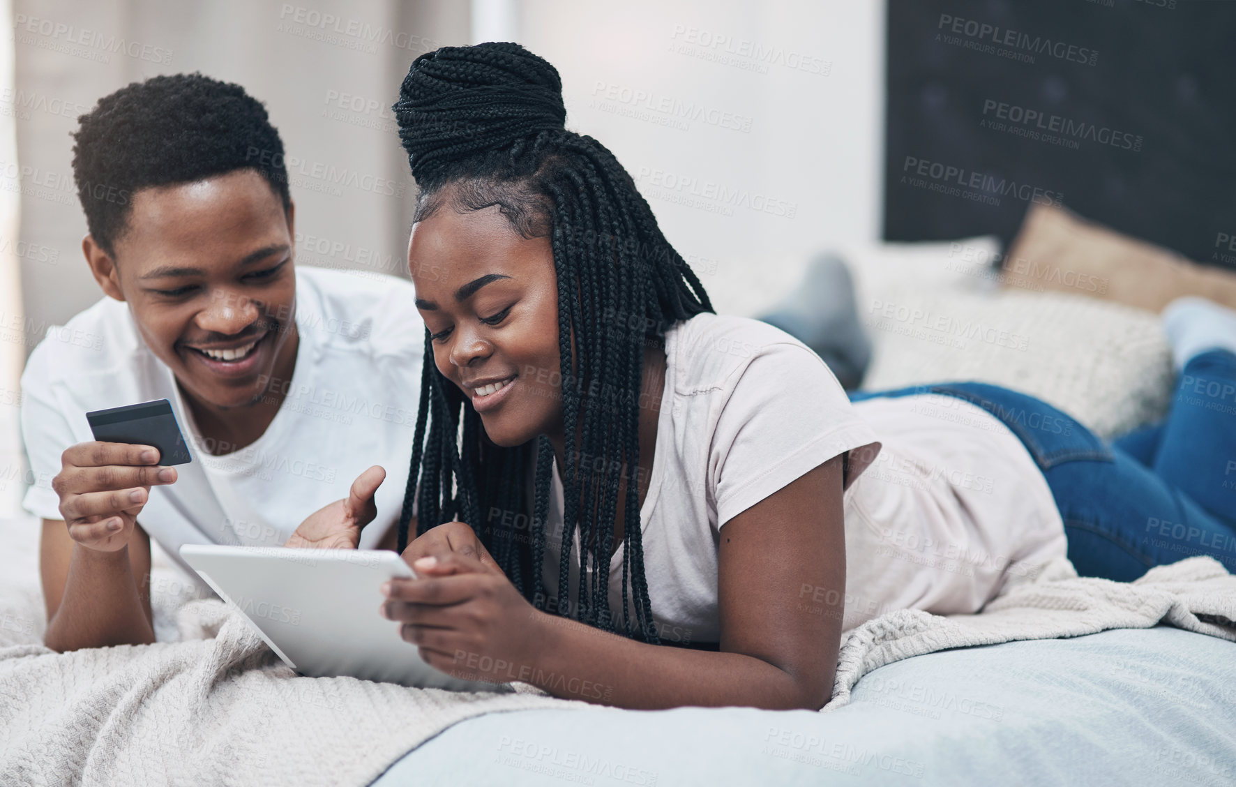 Buy stock photo Shot of a young couple using a digital tablet and credit card while relaxing on their bed at home