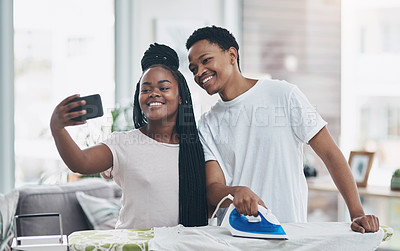 Buy stock photo Shot of a happy young couple taking selfies while ironing freshly washed laundry together at home