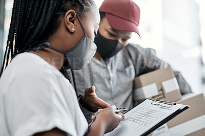 Buy stock photo Shot of a masked young woman signing for a delivery received at home