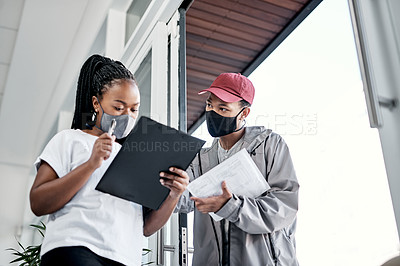 Buy stock photo Shot of a masked young woman signing for a delivery received at home
