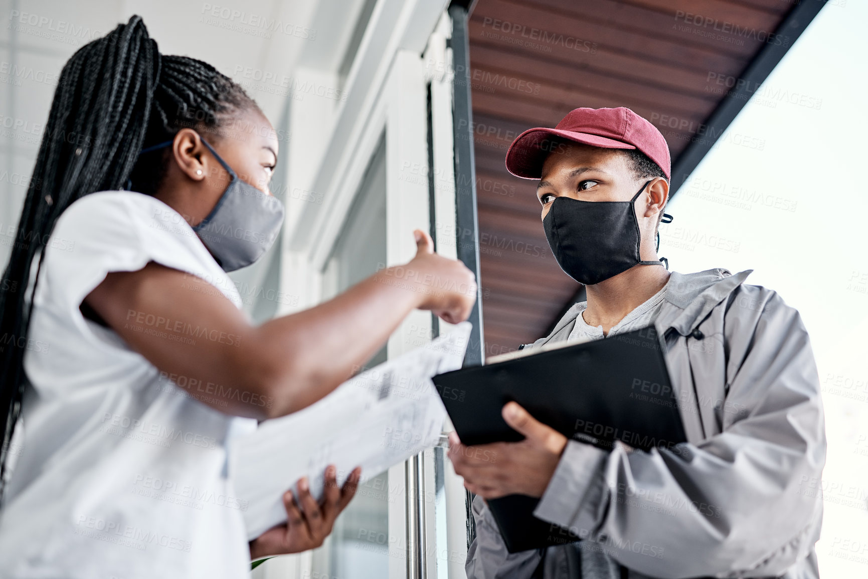 Buy stock photo Shot of a masked young woman showing thumbs up after receiving a delivery at home