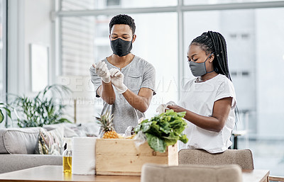 Buy stock photo Shot of a masked young couple disinfecting their groceries at home