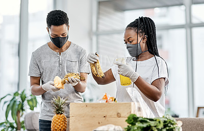 Buy stock photo Shot of a masked young couple disinfecting their groceries at home