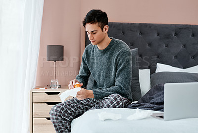 Buy stock photo Shot of a young man taking medication while recovering from an illness in bed at home