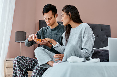 Buy stock photo Shot of a young couple taking medication while recovering from an illness in bed at home