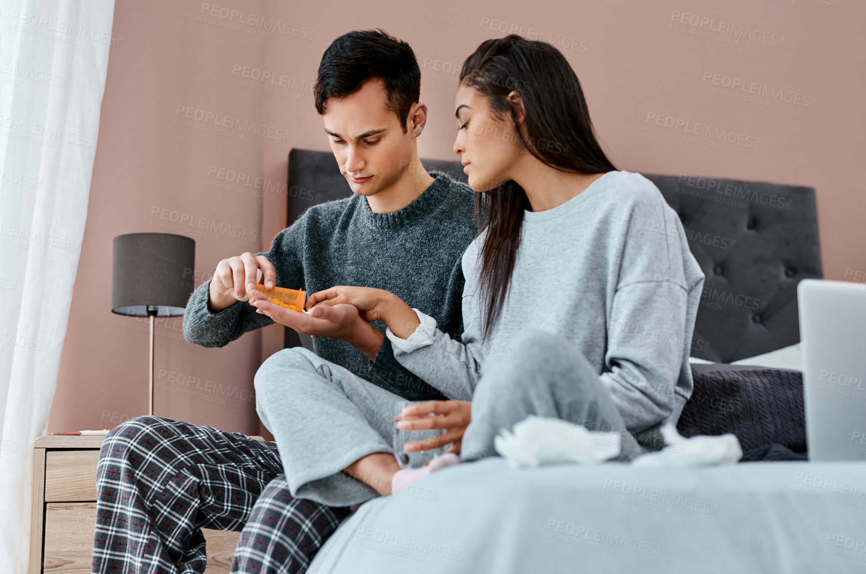 Buy stock photo Shot of a young couple taking medication while recovering from an illness in bed at home