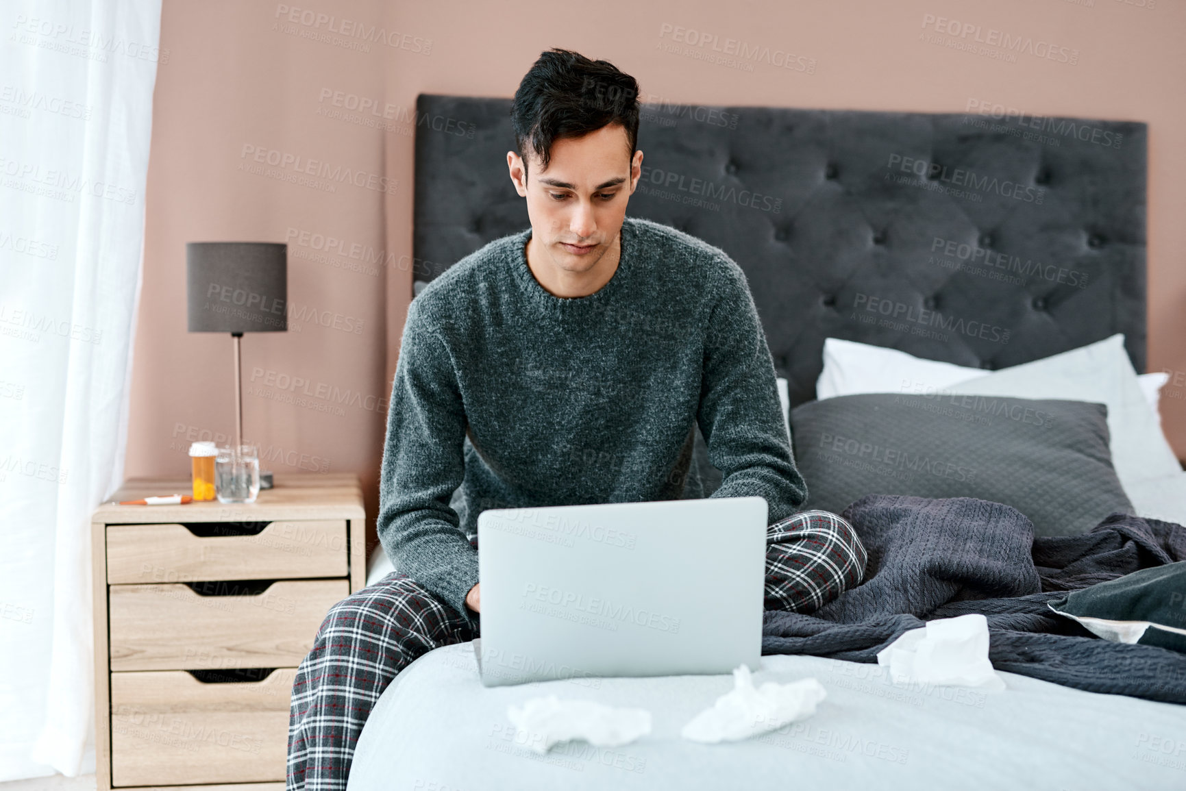 Buy stock photo Shot of a young man using a laptop while recovering from an illness in bed at home