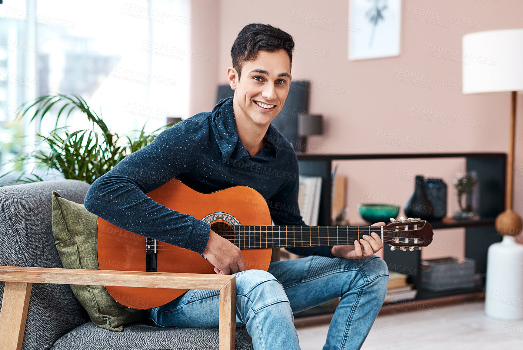 Buy stock photo Portrait of a young man playing a guitar at home