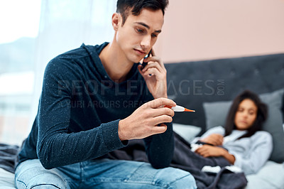 Buy stock photo Shot of a young man using a smartphone and thermometer while recovering from an illness with his wife at home