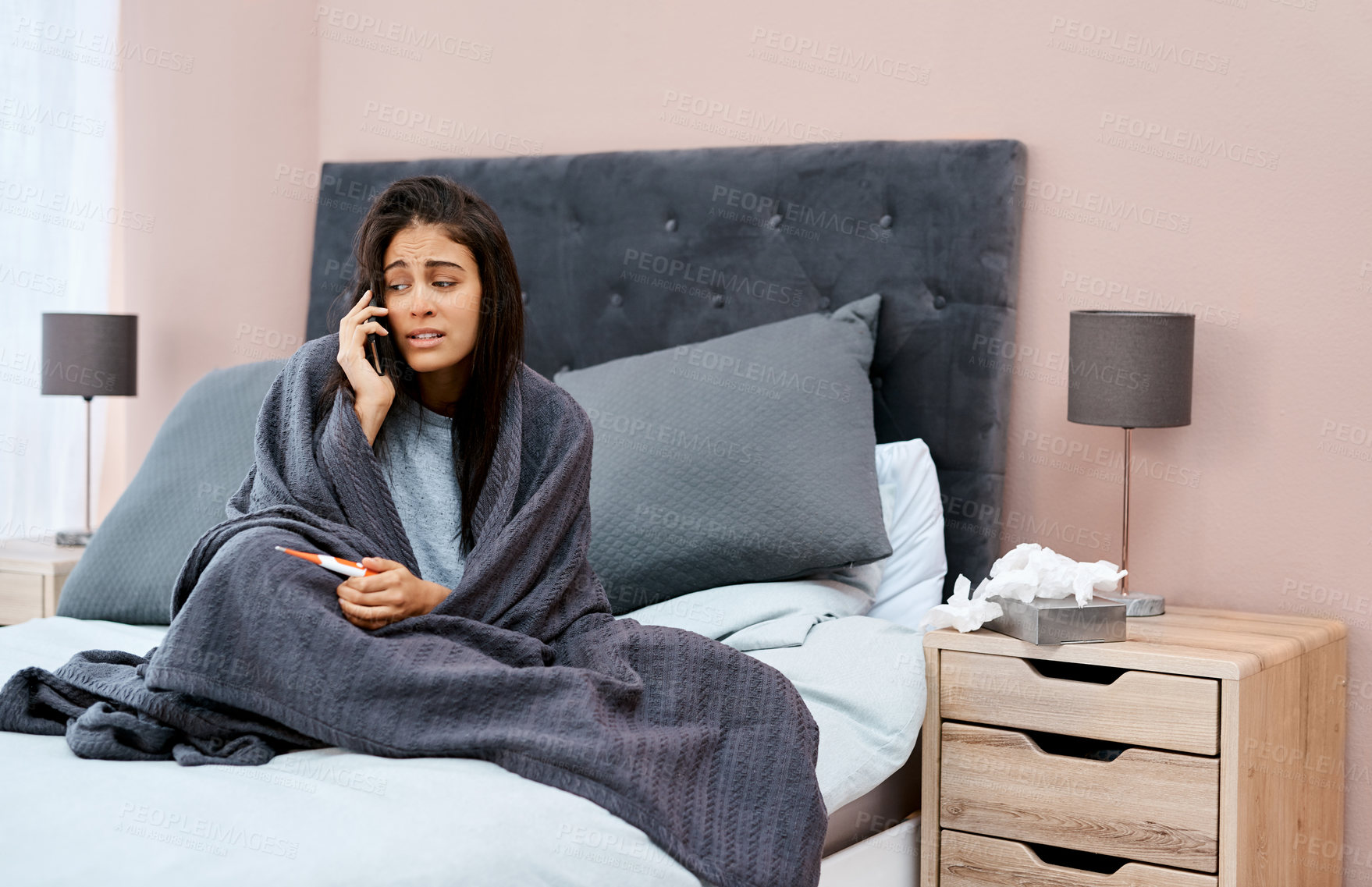 Buy stock photo Shot of a young woman using a smartphone and thermometer while recovering from an illness at home