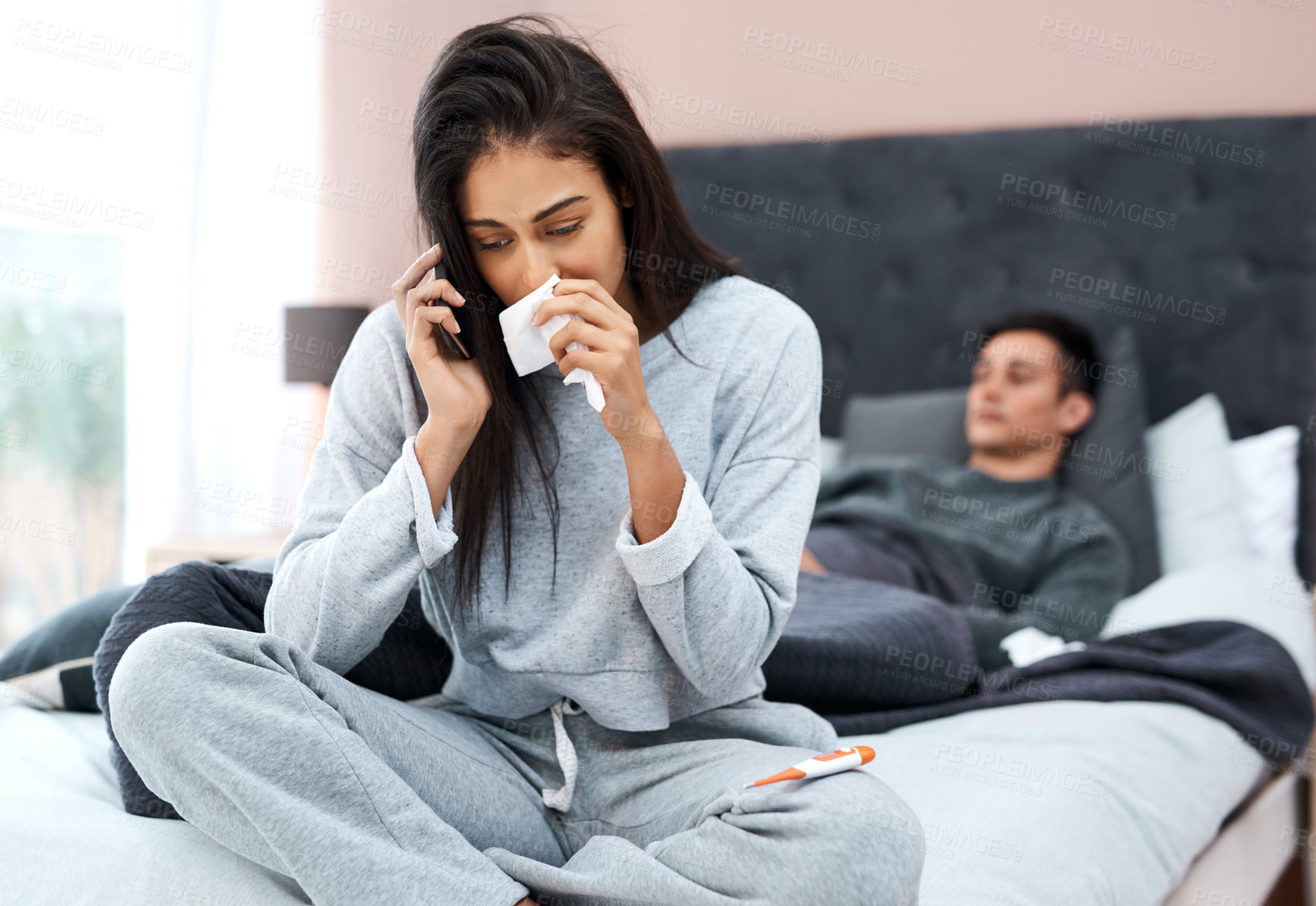 Buy stock photo Shot of a young woman using a smartphone while recovering from an illness with her husband at home