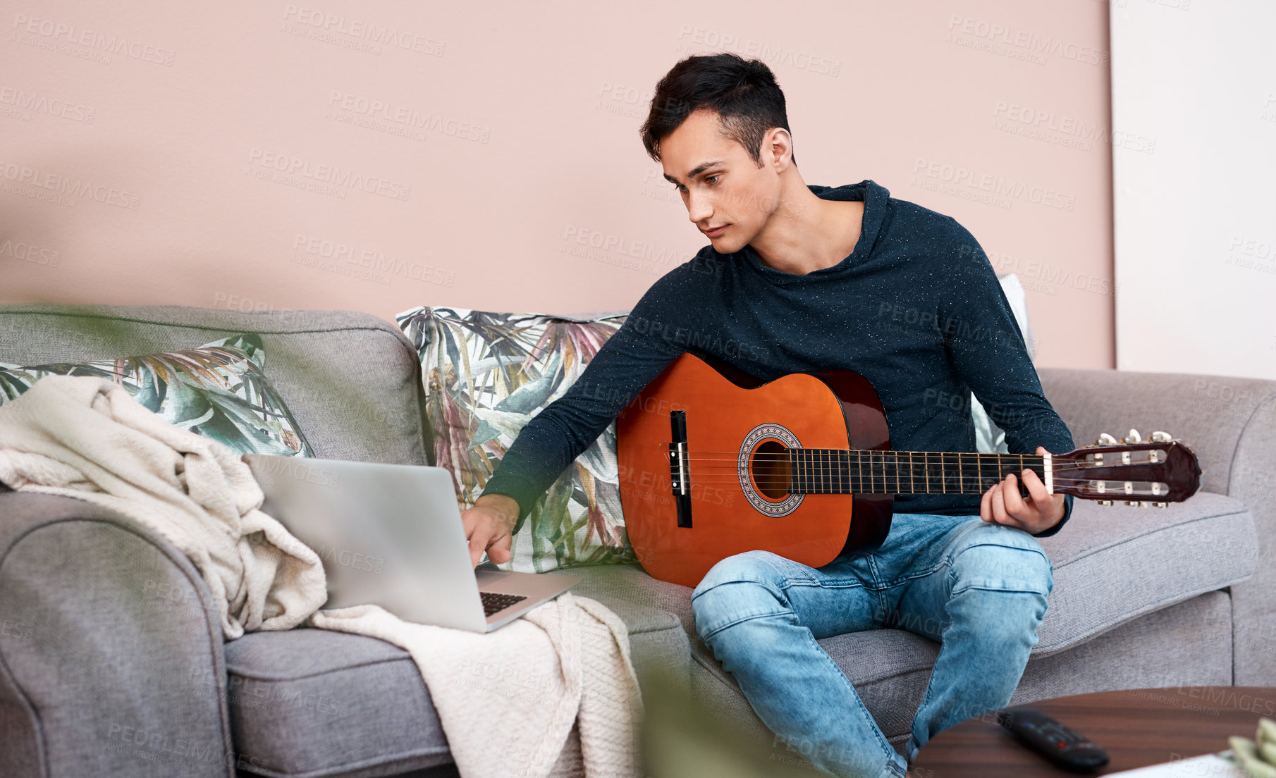 Buy stock photo Shot of a young man using a laptop while playing the guitar at home