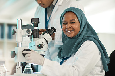 Buy stock photo Portrait of a young scientist using a microscope while working alongside a colleague in a lab