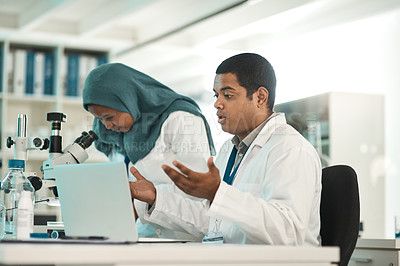 Buy stock photo Shot of a young scientist looking shocked while working on a laptop alongside a colleague in a lab