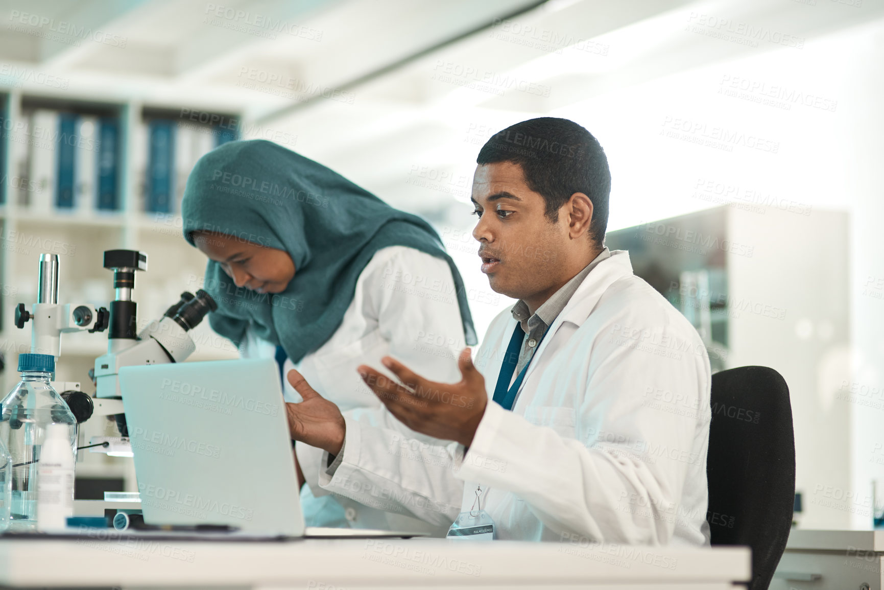 Buy stock photo Shot of a young scientist looking shocked while working on a laptop alongside a colleague in a lab