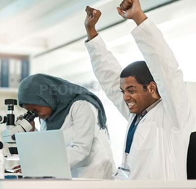 Buy stock photo Shot of a young scientist cheering while working on a laptop alongside a colleague in a lab