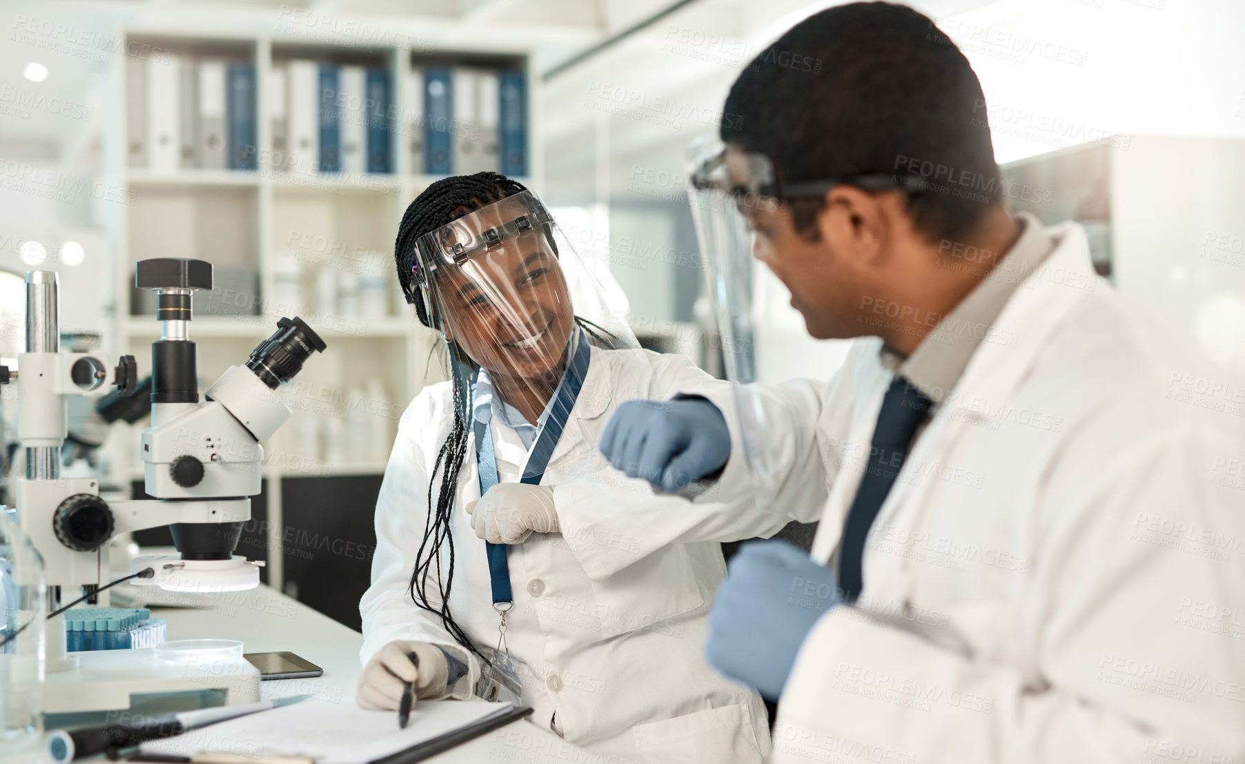 Buy stock photo Shot of two scientists bumping elbows while working together in a lab