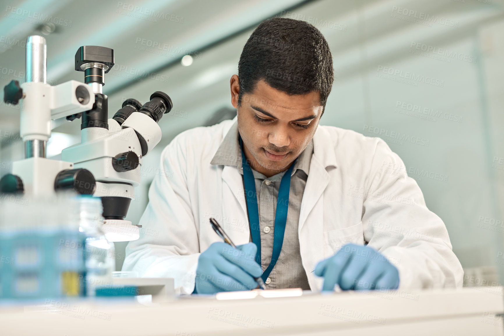 Buy stock photo Shot of a young scientist writing notes while working in a lab