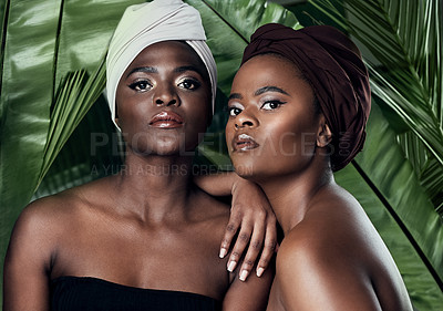 Buy stock photo Studio portrait of two beautiful young women posing in front of palm leaves against a grey background