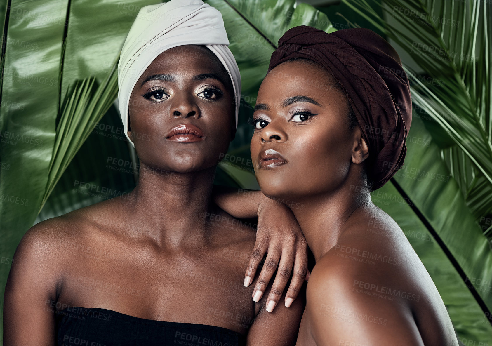 Buy stock photo Studio portrait of two beautiful young women posing in front of palm leaves against a grey background