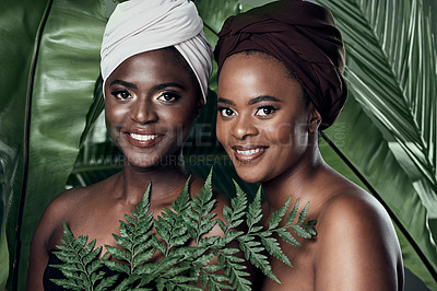 Buy stock photo Studio portrait of two beautiful young women posing in front of palm leaves against a grey background