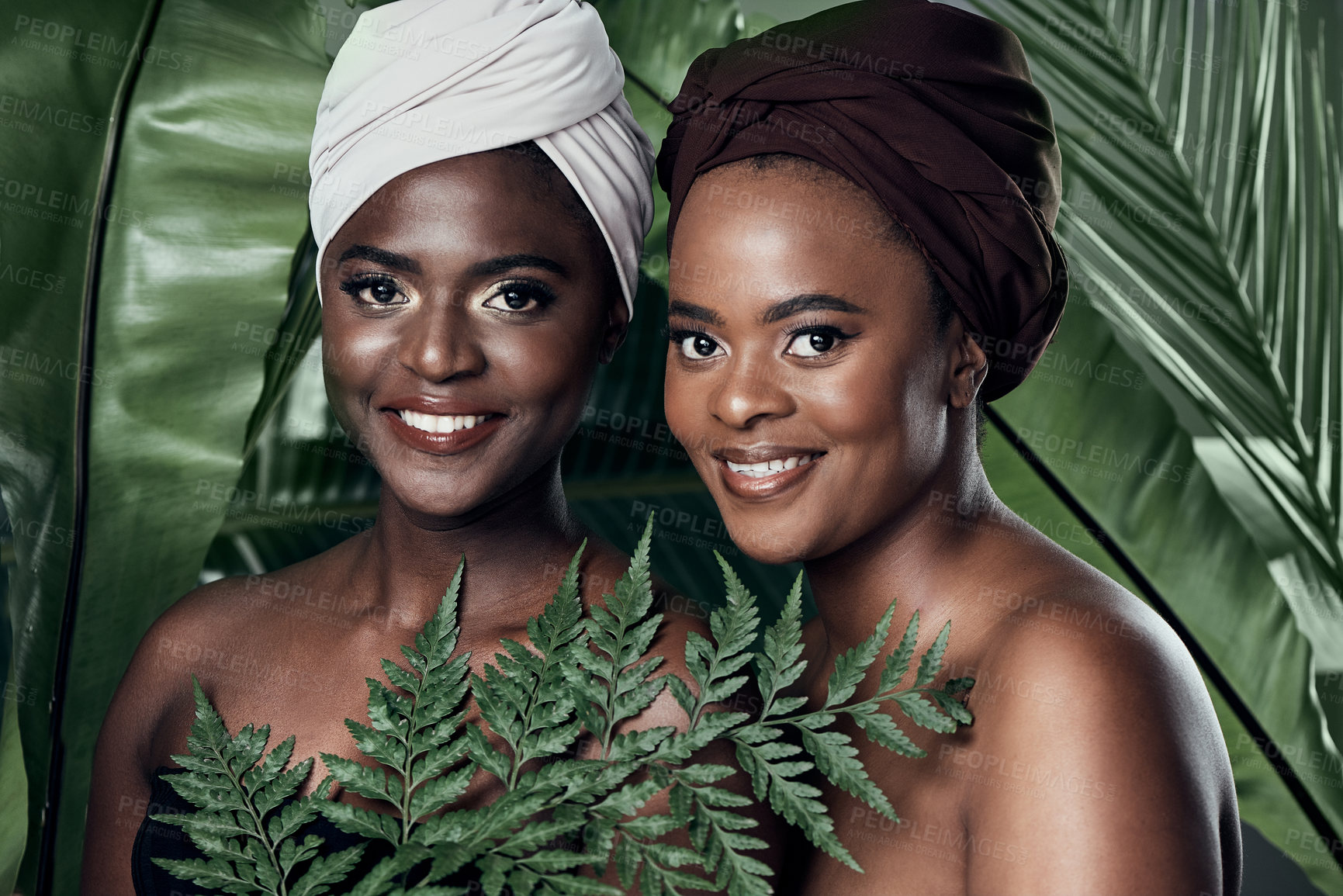 Buy stock photo Studio portrait of two beautiful young women posing in front of palm leaves against a grey background