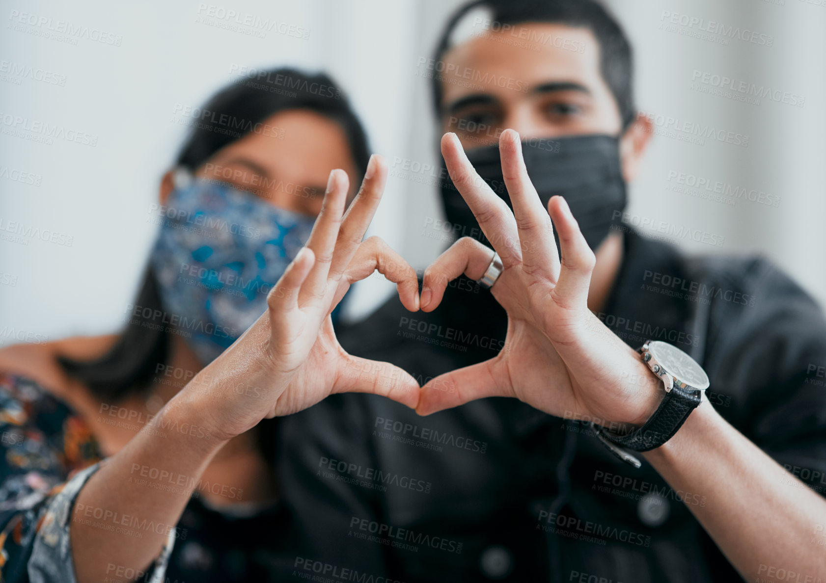 Buy stock photo Shot of a masked young couple making a heart shaped gesture with their hands at home