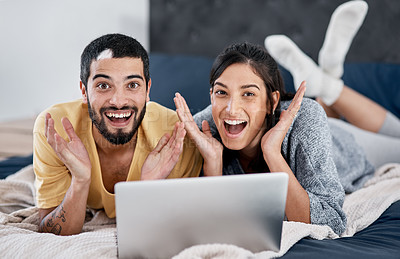 Buy stock photo Shot of a young couple using a laptop in bed and looking shocked