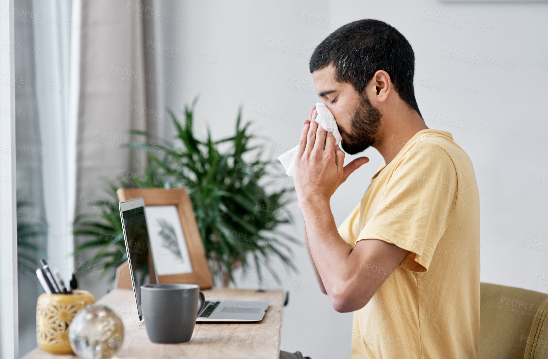 Buy stock photo Shot of a young man blowing his nose while working from home