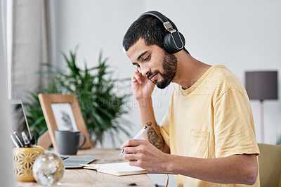 Buy stock photo Shot of a young man using a laptop and headphones while working from home