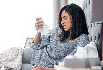 Buy stock photo Shot of a young woman blowing her nose while recovering from an illness in bed at home