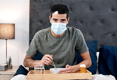 Buy stock photo Shot of a masked young man having breakfast in bed while recovering from an illness at home