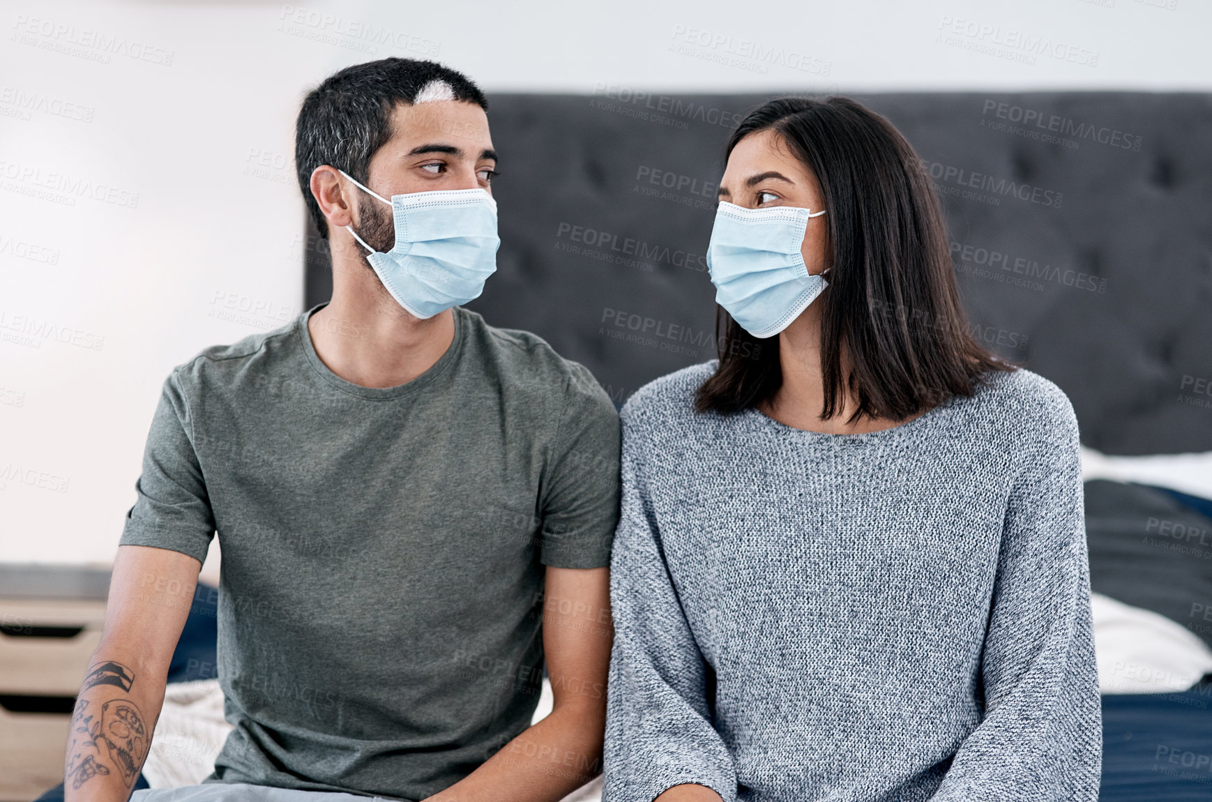 Buy stock photo Shot of a masked young couple recovering from an illness in bed at home