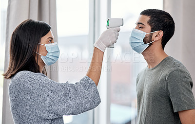 Buy stock photo Shot of a young woman taking her husband’s temperature while recovering from an illness at home