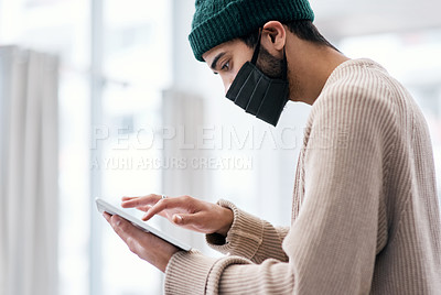 Buy stock photo Shot of a masked young man using a digital tablet while working from home