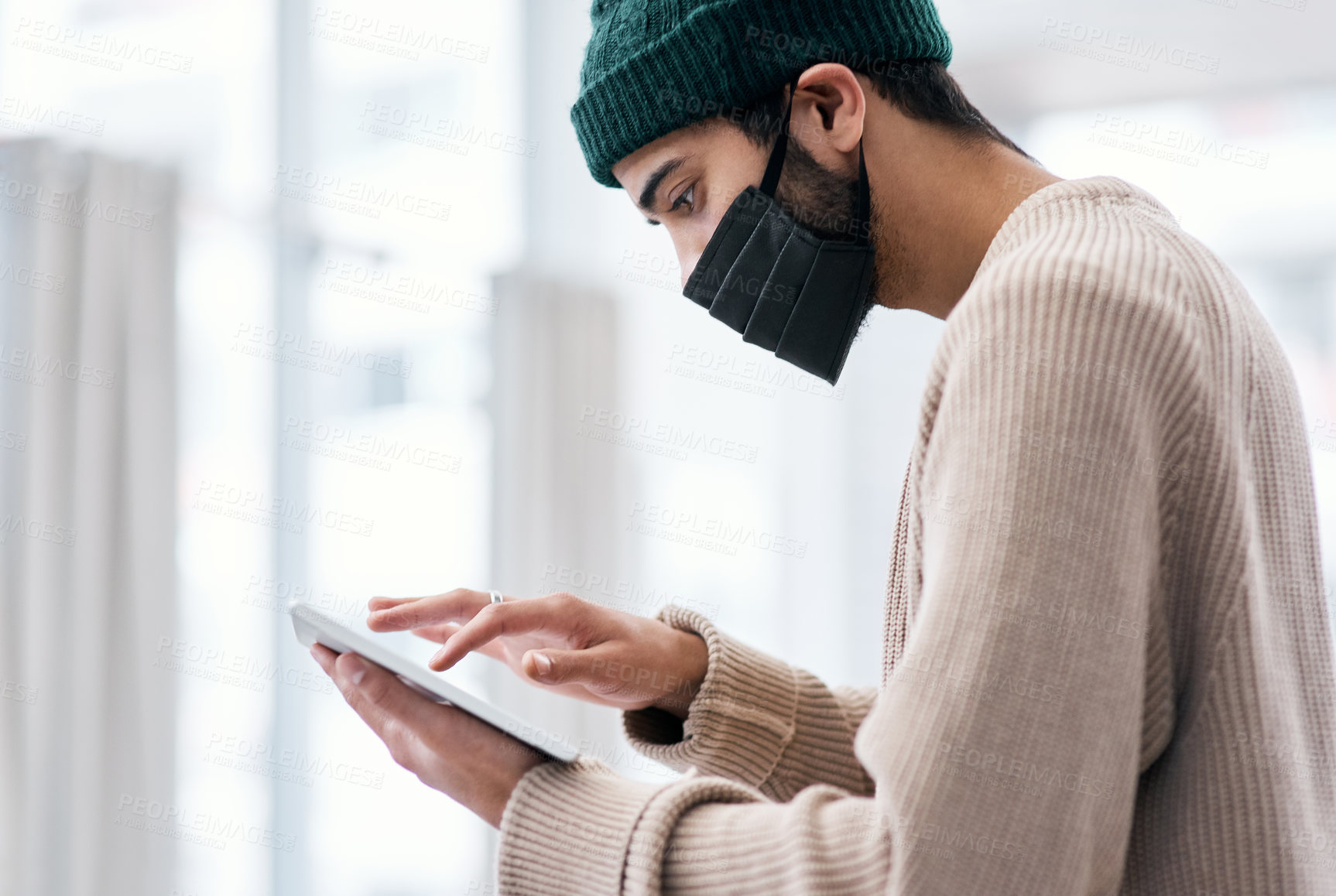 Buy stock photo Shot of a masked young man using a digital tablet while working from home