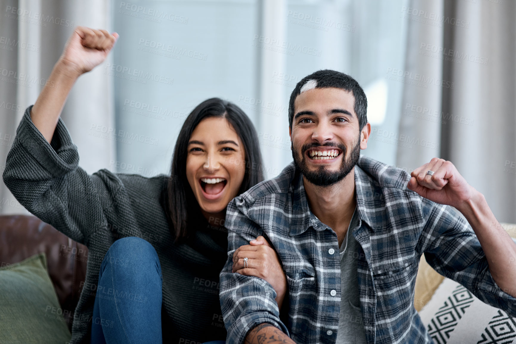 Buy stock photo Shot of a happy young couple watching tv and cheering at home