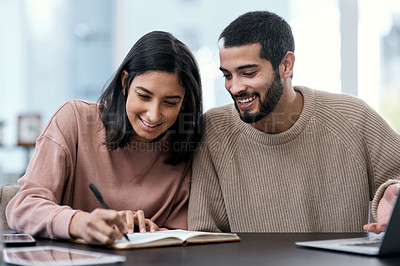 Buy stock photo Shot of a young couple going over notes together while working from home