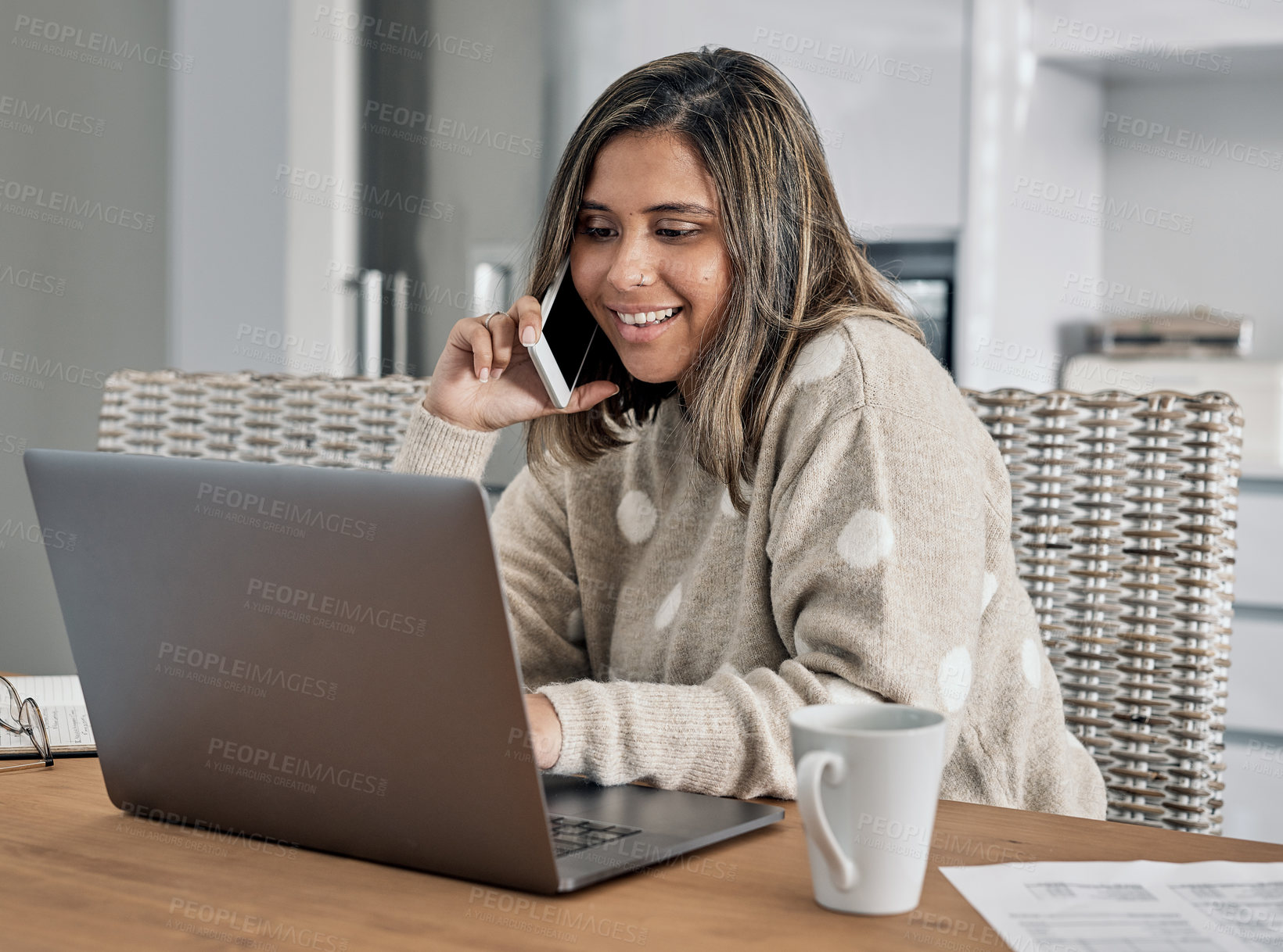 Buy stock photo Shot of a woman talking on her cellphone and using her laptop while working from home