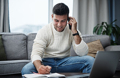 Buy stock photo Shot of a young man using a laptop and smartphone while writing in a notebook at home