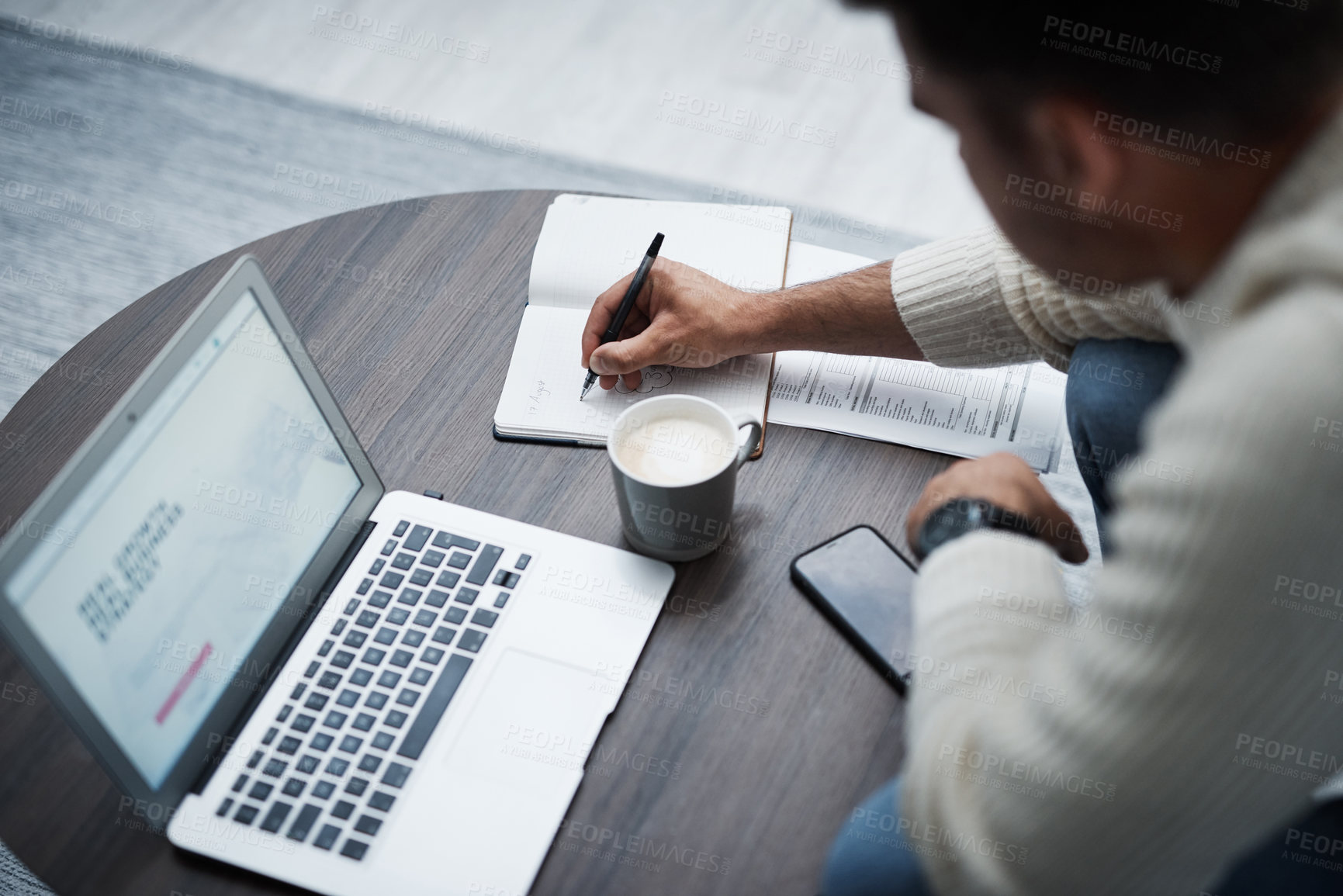 Buy stock photo Shot of a young man using a laptop and writing in a notebook while working from home