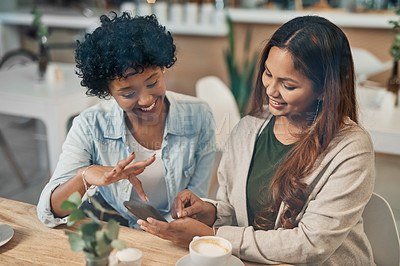 Buy stock photo Shot of two friends looking at something on a cellphone while sitting together in a coffee shop