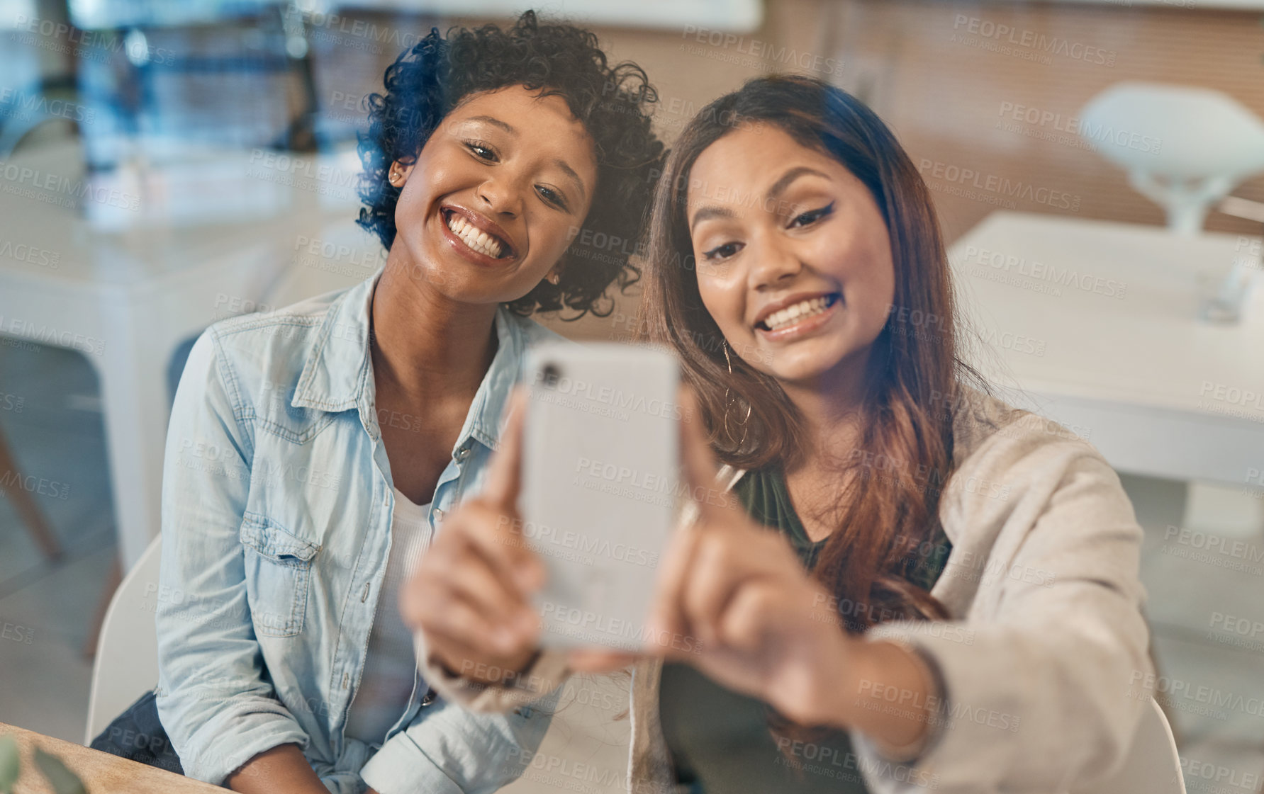 Buy stock photo Shot of two friends taking a selfie while sitting together in a coffee shop