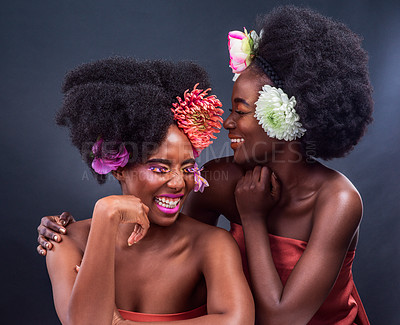 Buy stock photo African women, studio and laughing, flowers and afro hair for cosmetics, smile and confidence. Makeup, dark background and fashion for skincare, hairstyle and beauty or gossip, creative and style