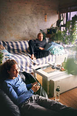 Buy stock photo Shot of a young woman playing video games while her boyfriend relaxes on the sofa in the background