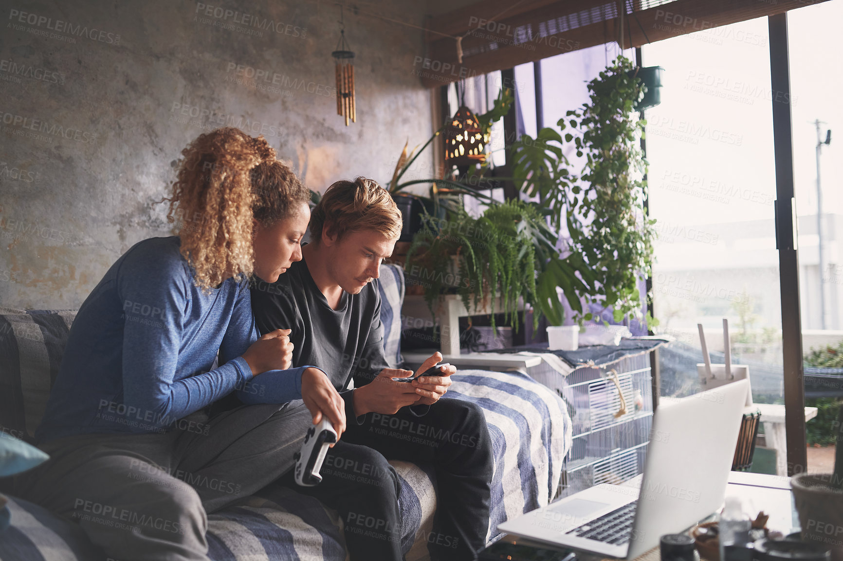 Buy stock photo Shot of a young couple using a smartphone while playing computer games on the sofa at home