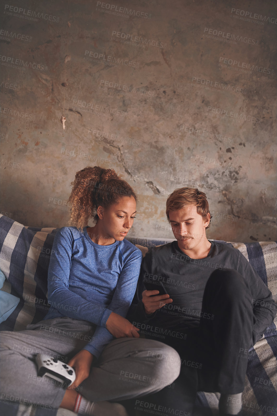 Buy stock photo Shot of a young couple using a smartphone while playing video games on the sofa at home