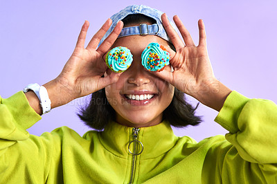 Buy stock photo Studio shot of a young woman holding cupcakes over her eyes against a purple background